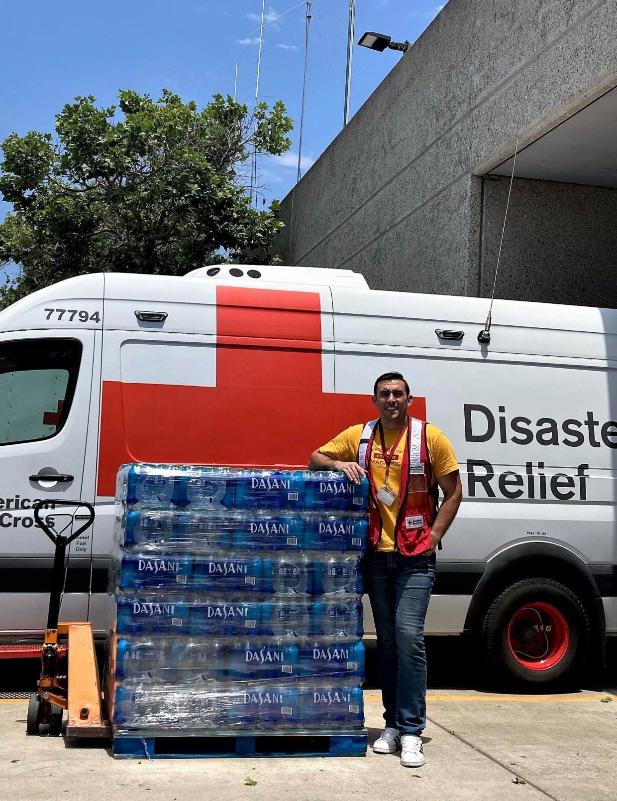 Photo of man standing with a pallet of water "Dasani" in front of a disaster relief van